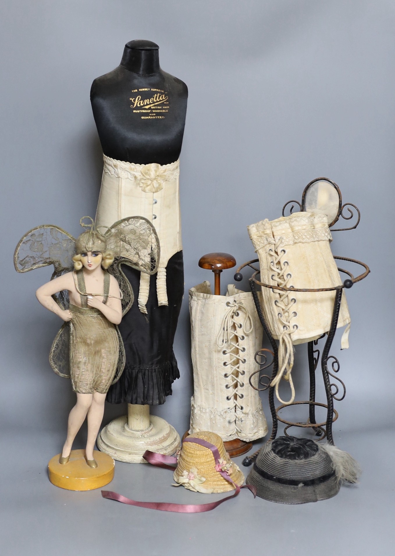 A 1920s/1930s ‘Sanetta’ shop display miniature corset dummy, 59 cm, three miniature corsets, a 1920s painted composition and metal thread decorated butterfly girl figure and other items